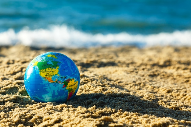 Bol van de aarde op een zandig strand op een oceaanachtergrond.