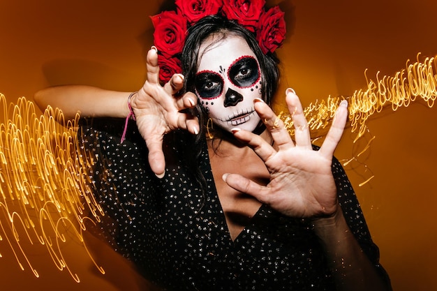 Bold curly darkhaired woman in halloween image posing at party Portrait of girl moving hands like sorceress