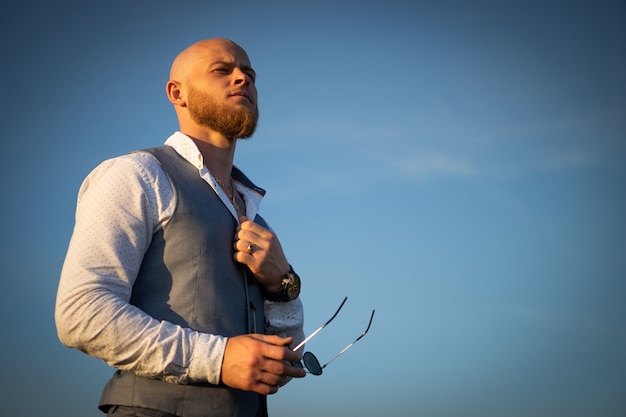 Foto ragazzo audace con un'elegante barba e occhiali da sole su un cielo durante il tramonto. concetto di successo e volontà.