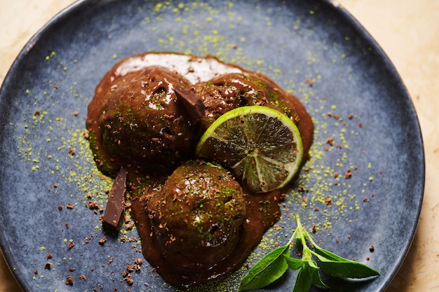 Bolletjes chocoladesorbet met besprenkeld groen matchapoeder schijfje limoencitroenbasilicum op donkerblauw bord Plat gelegd