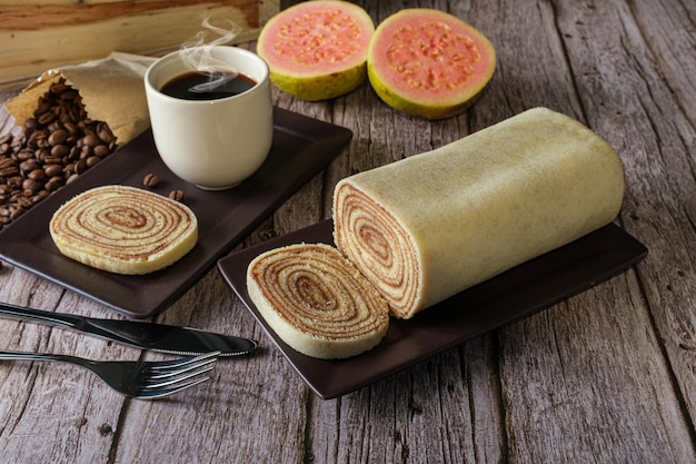 Bolo de rolo slice on a brown plate surrounded by cutlery and guava.