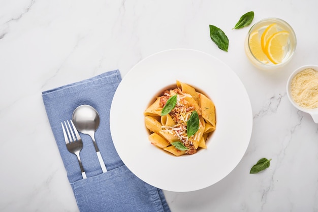 Bolognese penne pasta tasty appetizing classic italian penne
pasta with parmesan cheese basil and bolognese sauce in white plate
on plate on stone table traditional dish of italian cuisine top
view