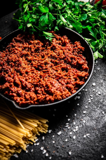 Bolognese sauce in a frying pan with pasta dry and parsley