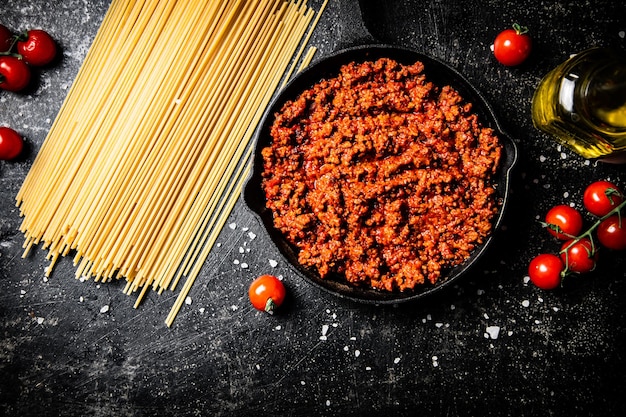 Bolognesesaus in een pan met tomaten en droge pasta