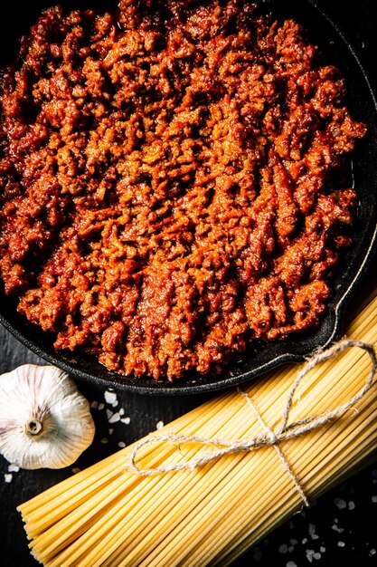 Foto bolognesesaus op een stenen bord met een bosje droge pasta en knoflook