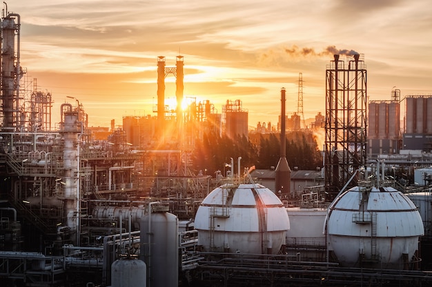 Boltanks voor gasopslag in de petrochemische industrie of olie- en gasraffinaderijfabriek 's avonds, productie van industriële petroleumfabriek met gaskolom en rookstapels op avondrood