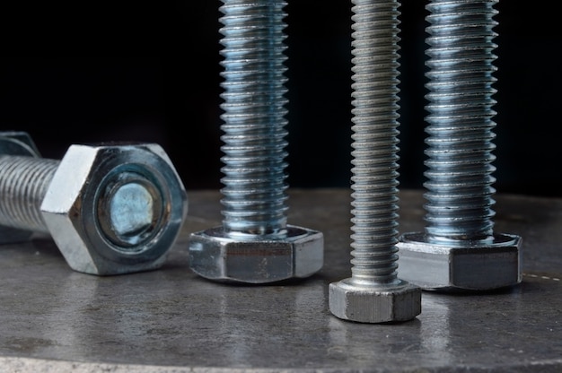Bolts and hex nuts of various sizes, laid out on a metal surface