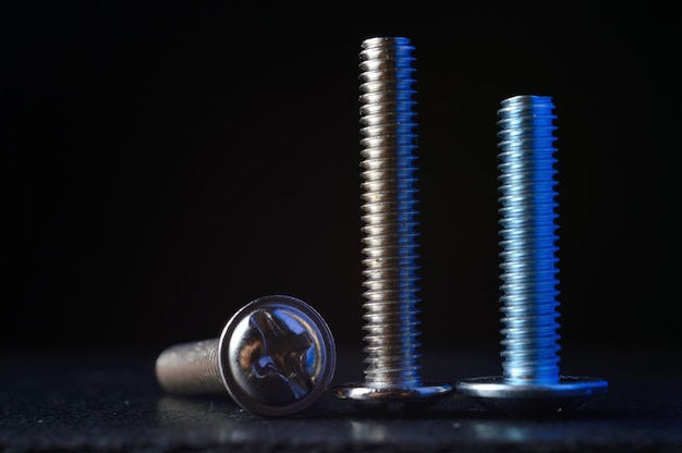 Bolts and screws of different sizes and threads stand on a dark surface. dark background. close-up.
