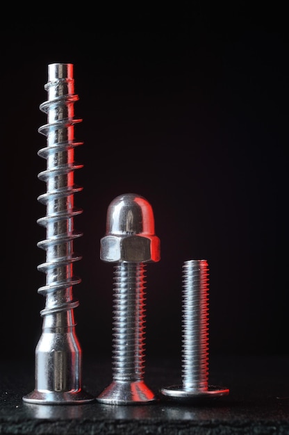 bolts and screws of different sizes and threads stand on a dark surface. dark background. close-up.