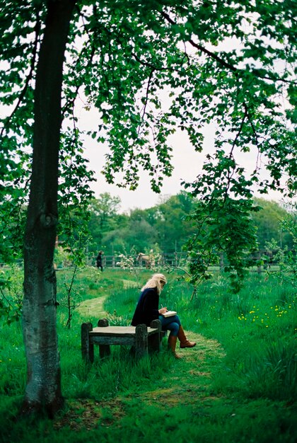 Bomen en lang gras een gemaaid pad een vrouw zittend op een houten stoel