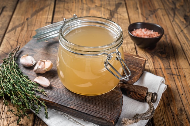 Bone broth for chicken soup in a glass jar. Wooden background. Top view.