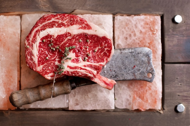 Bone in rib eye row steak on pieces of salt on wooden board