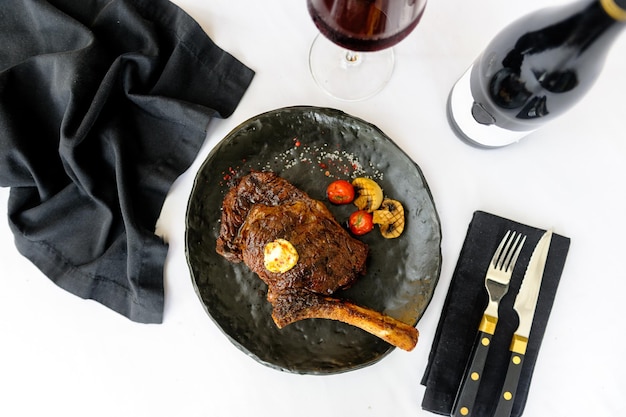 Bonein beef steak on a black plate with a glass of wine