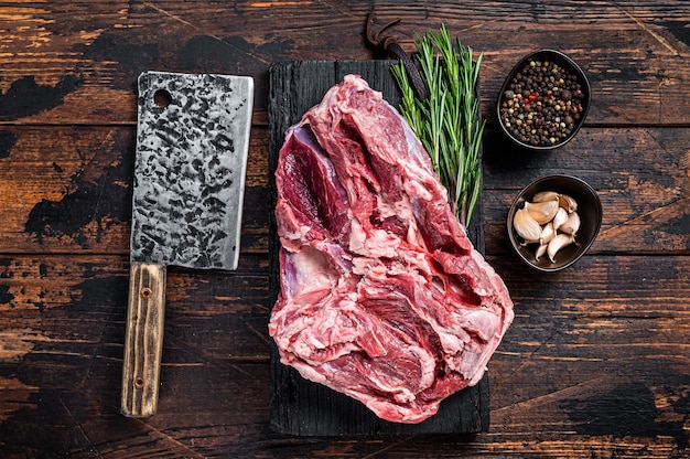 Boneless raw Leg of mutton Lamb meat on butcher cutting board with cleaver. Dark wooden background. Top view.