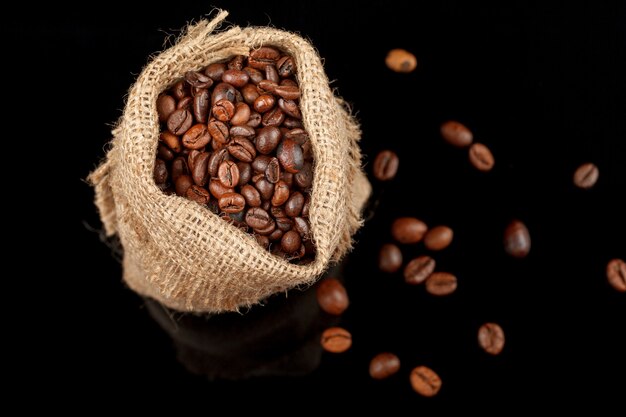 Bonen geroosterde koffie in een zak, close-up op zwarte achtergrond.