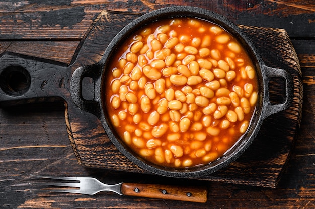 Bonen in tomatensaus in een pan. Donkere houten achtergrond. bovenaanzicht.