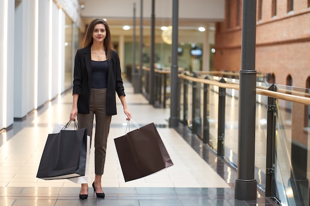 Boodschappen doen. Aantrekkelijke jonge vrouw, gekleed in modieuze kleding met grote papieren boodschappentassen wandelen na het winkelen.