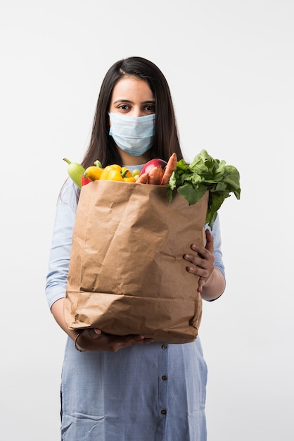 Boodschappen doen in Pandemic - Mooie Indiase jonge vrouw die een beschermend masker draagt terwijl ze een papieren zak met groenten en fruit vasthoudt tijdens een virusepidemie