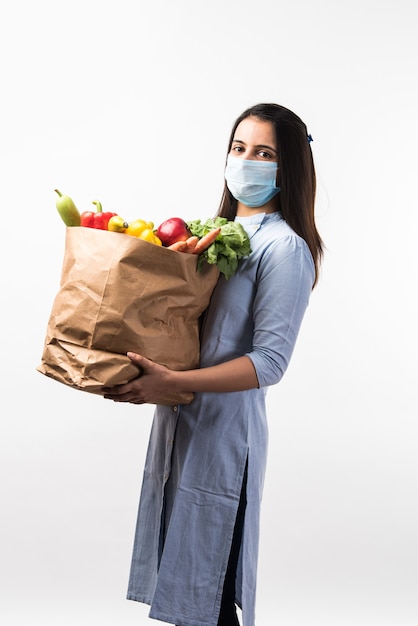 Boodschappen doen in Pandemic - Mooie Indiase jonge vrouw die een beschermend masker draagt terwijl ze een papieren zak met groenten en fruit vasthoudt tijdens een virusepidemie