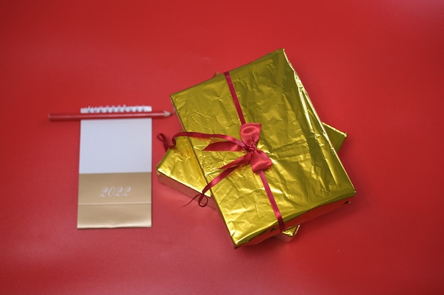 Boodschappenlijstje en cadeaus voor 2022. Cadeau in een gouden doos op een rode achtergrond.