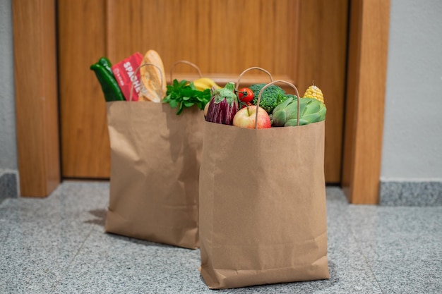Boodschappentassen voor eten staan voor de deur van het huis of appartement Bezorging van groenten en fruit tijdens quarantaine en zelfisolatie