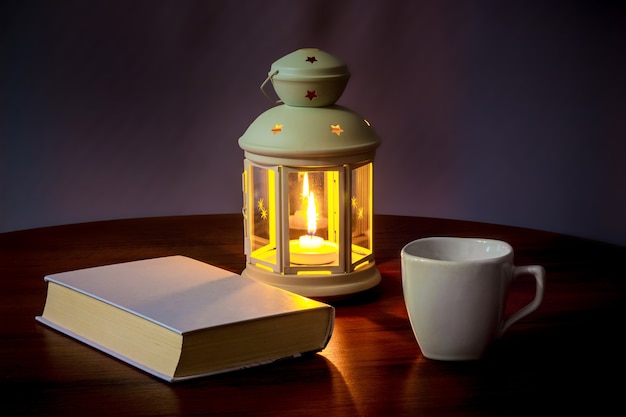 A book and a cup of coffee in the light of a lantern with a candle in the evening 