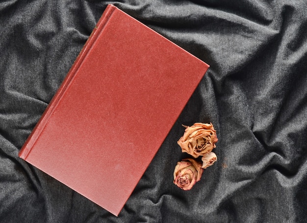 A book and dried roses on a gray fabric background. Top view.