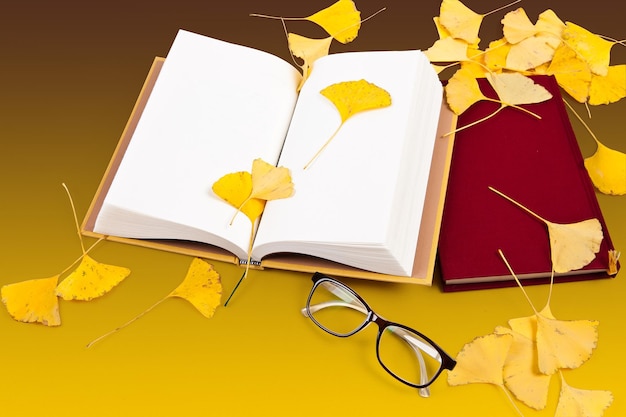 A book and glasses on a table with leaves on the table