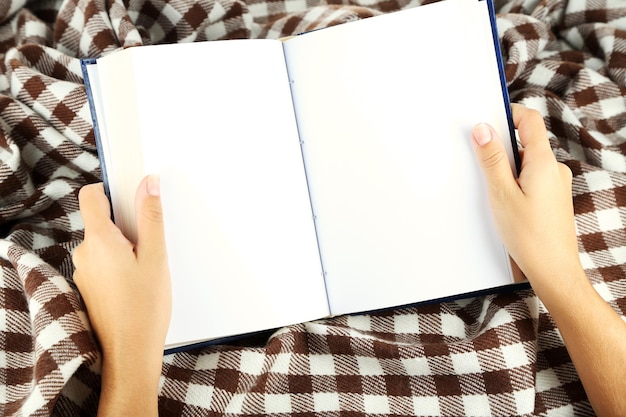 Book in hands on plaid background