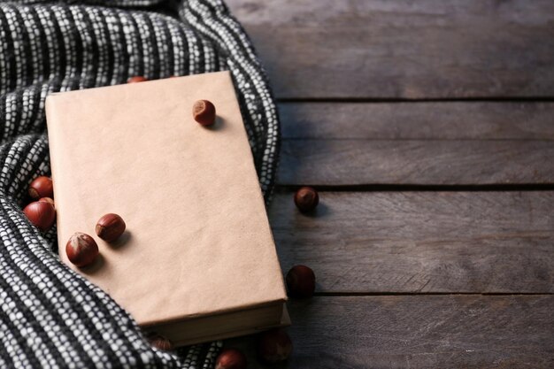 A book hazelnuts and a woolen blanket on wooden background