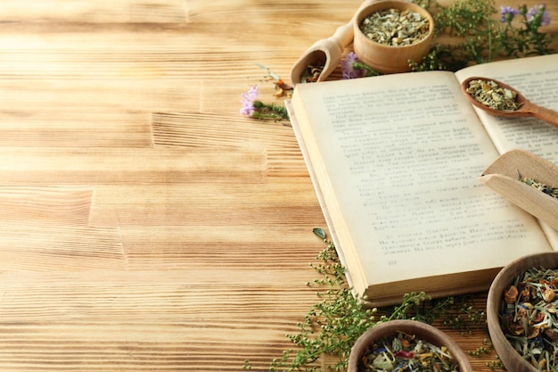 Book herbs in bowls and scoops on wooden background space for text