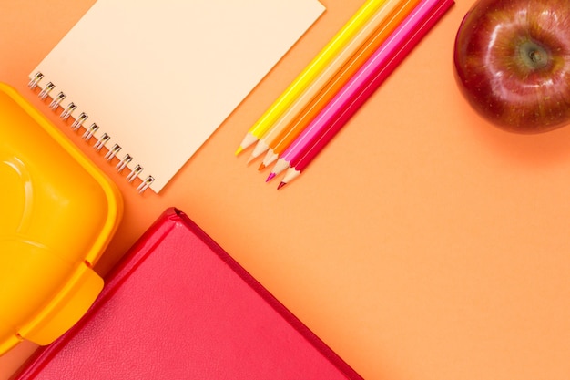 Book, lunch box, notebook, color pencils and apple on pink background. top view. back to school concept. school supplies. pastel colors