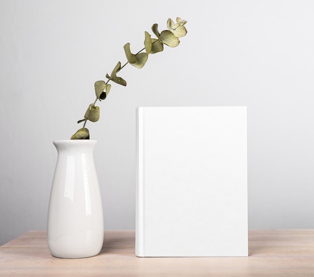 Prenota mockup e fiori in vaso al tavolo di legno stile minimalista lettura per il tempo libero armonia lettore concetto di stile di vita romanzo con copertina bianca