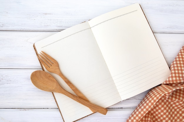  book notepad paper and tablecloth with wooden fork and spoon on white table