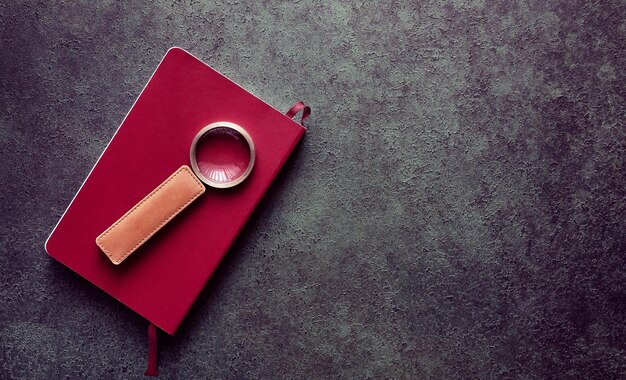 Photo book in red cover and magnifying glass, vintage toned background with copy space