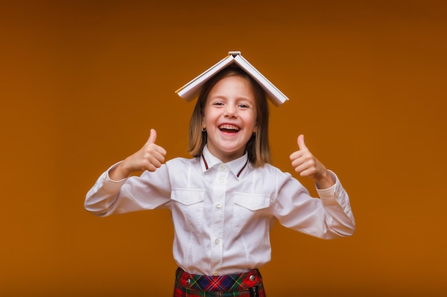 あなたの頭の上の本の屋根小さな女の子が彼女の頭に教科書を持っていますオレンジ色の背景に本を持った小さな女の子