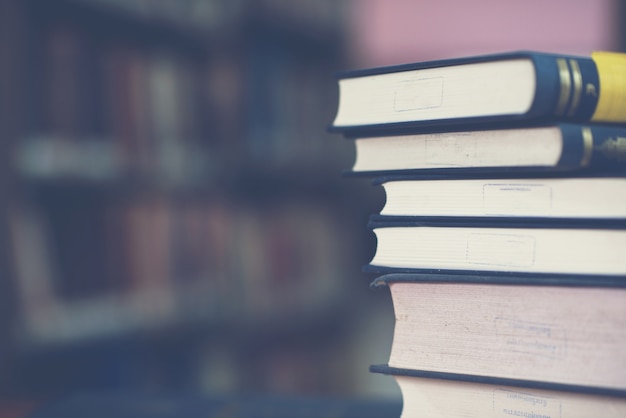 Book stack on wood desk and blurred bookshelf in the library room, education background