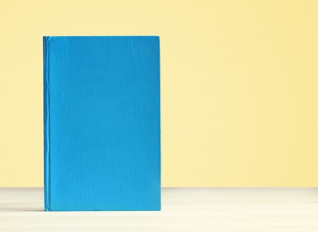 Book with blue blank cover on the table on a yellow background. 