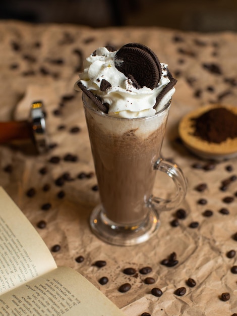 A book with a book open to the right of a glass of coffee with oreo cookies on top.