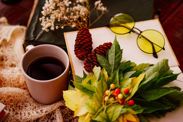 Book with glasses cup and books maple leaves on wooden table side view fall season