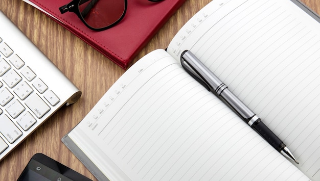 book with pen, mobile and keyborad on desk