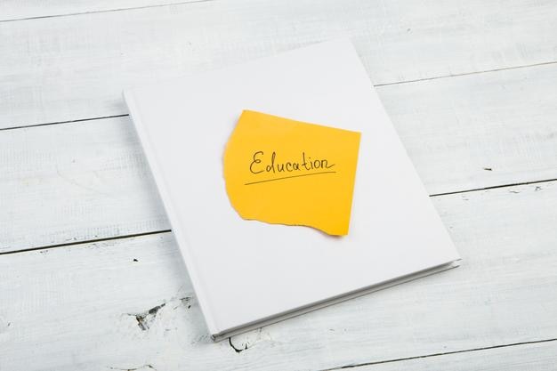 Book and yellow sheet with education inscription on a white wooden desk