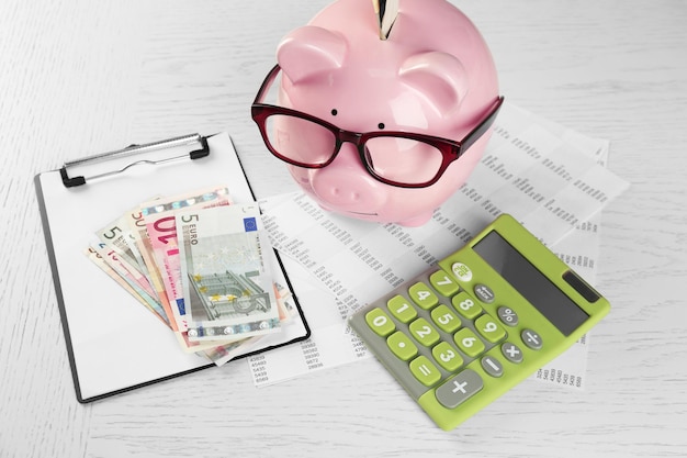 Bookkeeping concept Piggy bank calculator euro and papers on white wooden background