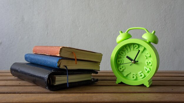 Photo books and alarm clock against wall on table