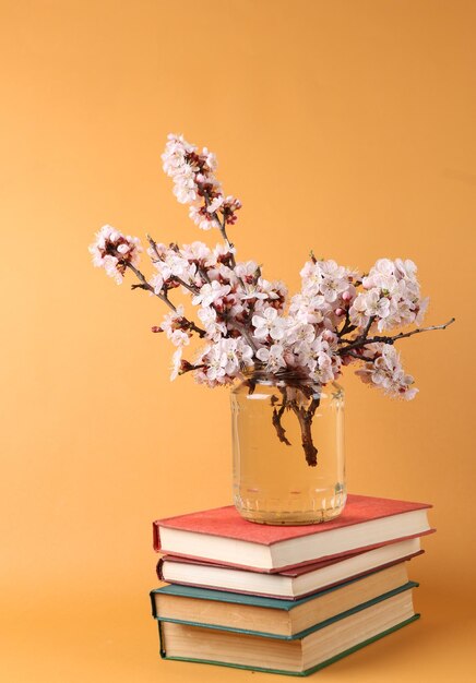 Books and Beautiful flowering branches in glass jar on brown background