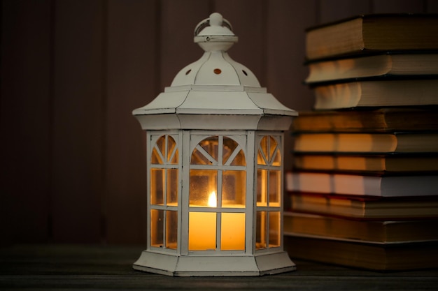 Books and decorative lantern on table and wooden planks background