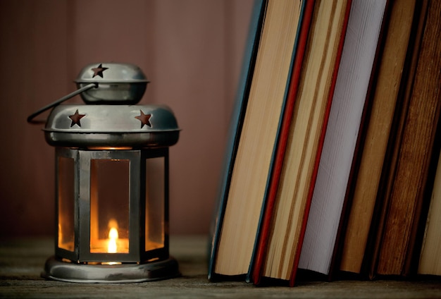 Books and decorative lantern on table and wooden planks background