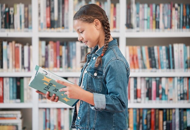 Books education or child in a library reading for knowledge or development for future growth Scholarship girl or school student with a happy smile studying or learning information in a fun story