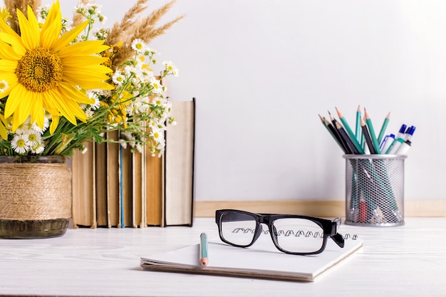 Books, glasses, markers and a bouquet of flowers in a vase on white 