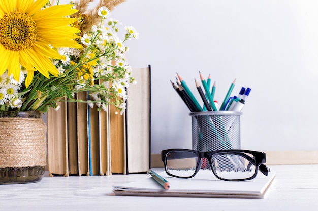 Libri, bicchieri, pennarelli e un mazzo di fiori in un vaso su bianco